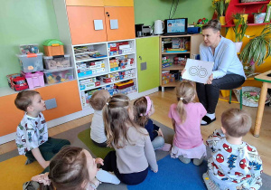 Pedagog specjalny pokazuje dzieciom symbol osób w spektrum autyzmu- znak nieskończoności