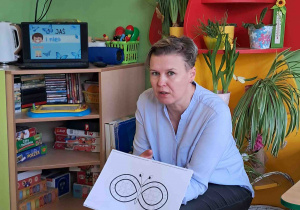 Pedagog specjalny pokazuje dzieciom symbol osób w spektrum autyzmu- znak nieskończoności