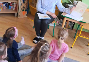 Dzieci siedzą na dywanie i słuchają bajki czytanej przez pedagoga
