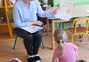 Dzieci siedzą na dywanie i słuchają bajki czytanej przez pedagoga
