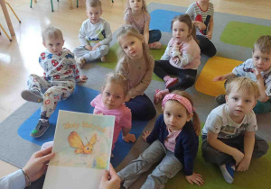 Dzieci siedzą na dywanie i słuchają bajki czytanej przez pedagoga