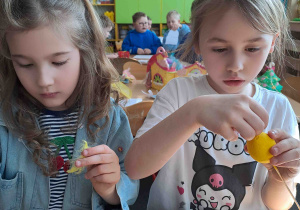 Dzieci wykonują kurczątka z wcześniej pomalowanych jajeczek, piórek i pianki plastycznej