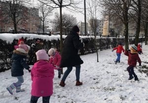 Dzieci wraz z Panią rzucają się śnieżkami.