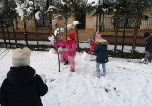 Troje dzieci toczy kulę śniegową.