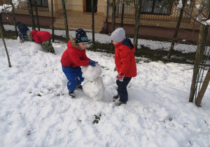 Dwóch chłopców próbuje postawić bałwanka. Na razie ułożyli dwie kule śniegowe..