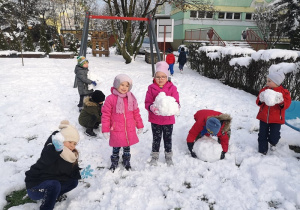 Dzieci pozują do zdjęcia trzymając kulki śniegowe.