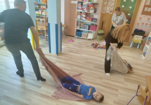 Rodzice ciągną dzieci na kocach po podłodze