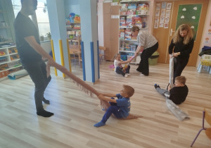Rodzice ciągną dzieci na kocach zwiniętych w rulon