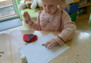 Dziewczynka wykonuje prace plastyczną - biedronke