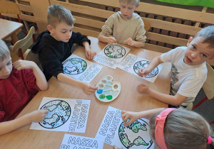 Dzieci wykonują pracę plastyczną przy użyciu farb i patyczków higienicznych tworząc obrazek ziemi