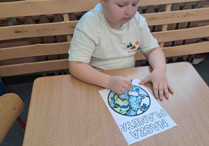 Dzieci wykonują pracę plastyczną przy użyciu farb i patyczków higienicznych tworząc obrazek ziemi