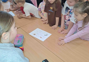 Dzieci przy stoliczkach rozwiązują rebusy słowno- obrazkowe