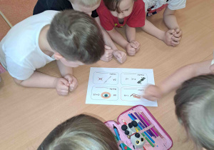 Dzieci przy stoliczkach rozwiązują rebusy słowno- obrazkowe
