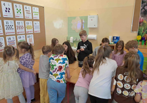 Dzieci przy stoliczkach rozwiązują rebusy słowno- obrazkowe
