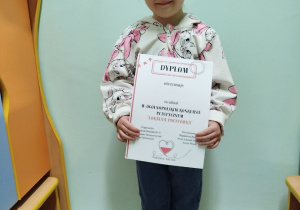 Dziewczynka pozuje do zdjęcia z dyplomem.