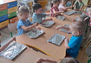 Dzieci wykonują eksperymenty przy stolikach