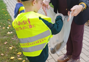 Dziecko w kamizelce odblaskowej wrzuca zebrane odpady do worka