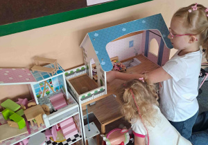 Dziewczynki ustawiają mebelki w domku dla lalek