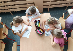 Dzieci przy stoliczkach kolorują wspólnie ilustrację