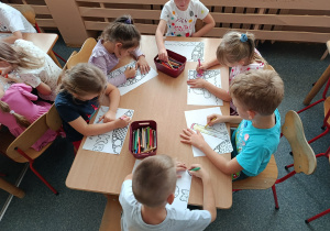 Dzieci przy stoliczkach kolorują wspólnie ilustrację