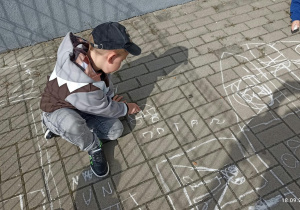 Chłopiec rysuje miasteczko kredą na chodniku