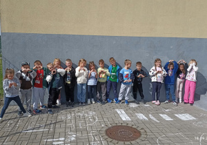 Dzieci stoją obok szkoły i prezentują swoje kredowe miasteczko
