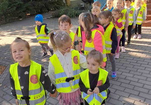 Dzieci w kamizelkach odblaskowych wybierają się na spacer na skrzyżowanie