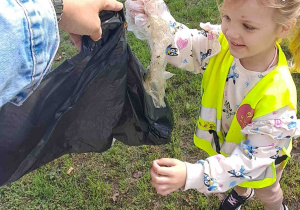 Dziecko wrzuca śmieci znalezione na trawniku do worka na śmieci
