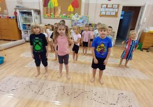 Dzieci z grupy "Poziomek" stoją boso w sali przedszkolnej przed rozpoczęciem sensorycznych zajęć plastycznych