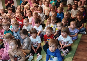 Dzieci siedzą na dywanie i uczestniczą w spotkaniu edukacyjnym