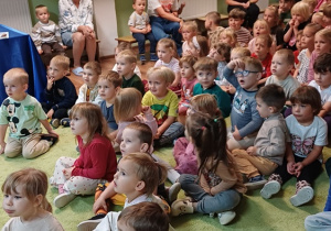 Dzieci siedzą na dywanie i uczestniczą w spotkaniu edukacyjnym