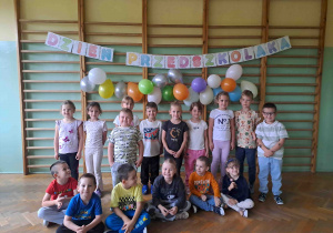 Pamiątkowa grupowa fotografia na tle napisu i balonów