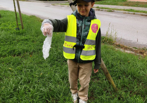 Chłopiec pokazuje, jaki śmieć znalazł na trawniku