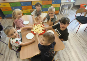 Dzieci przy stoliku próbują jabłka.