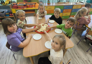 Dzieci przy stoliku próbują jabłka.