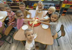 Dzieci przy stoliku próbują jabłka.