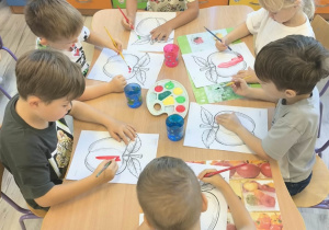 Dzieci przy stoliku maluja farbami.
