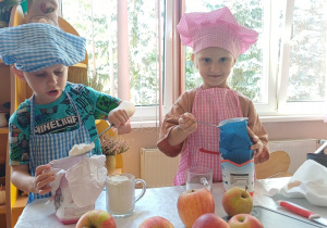 Dzieci w czapkach i fartuchach kucharskich przygotowują ciasto podczas zajęć kulinarnych