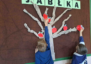 Dzieci umieszczają przygotowane wcześniej papierowe jabłuszka na drzewie
