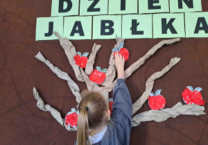 Dzieci umieszczają przygotowane wcześniej papierowe jabłuszka na drzewie