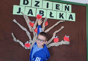 Dzieci umieszczają przygotowane wcześniej papierowe jabłuszka na drzewie