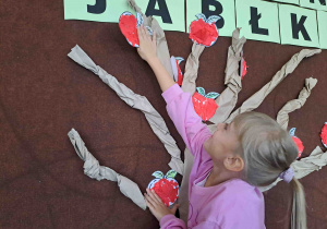 Dzieci umieszczają przygotowane wcześniej papierowe jabłuszka na drzewie