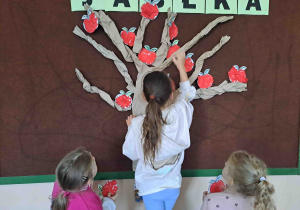 Dzieci umieszczają przygotowane wcześniej papierowe jabłuszka na drzewie