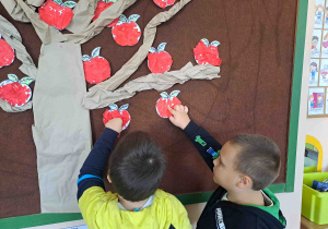 Dzieci umieszczają przygotowane wcześniej papierowe jabłuszka na drzewie