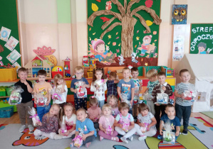 Grupa dzieci stoi na tle dekoracji z upominkami w ręku.