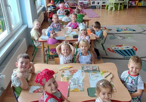 Dzieci siedzą przy stolikach w fartuszkach