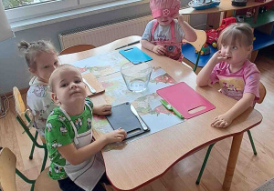 Dzieci siedzą przy stolikach w fartuszkach