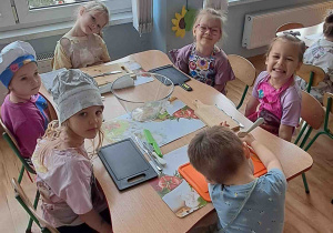 Dzieci siedzą przy stolikach w fartuszkach