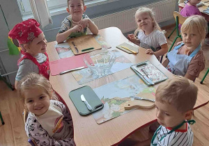 Dzieci siedzą przy stolikach w fartuszkach
