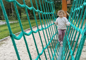 Dziewczynka idzie po równoważni w środku siatki wspinaczkowej
